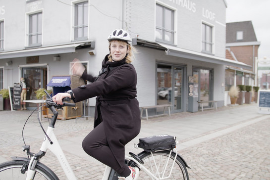 Eine blonde Frau mit weißen Sturzhelm fährt Fahrrad
